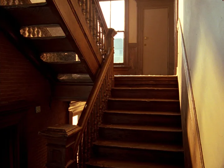 A wooden staircase with turned balusters rising to a landing, a plain door and a sunlit window at the top.