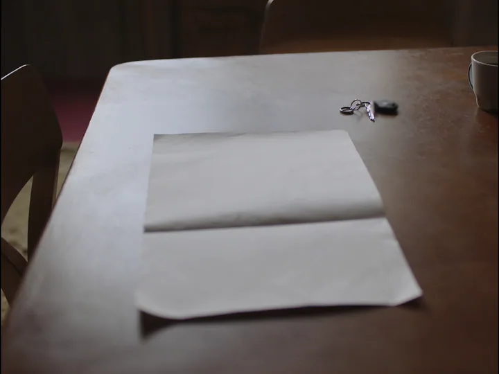 A folded blank sheet of paper on a dark wooden table, a ring of keys beside it and a coffee mug at the edge.